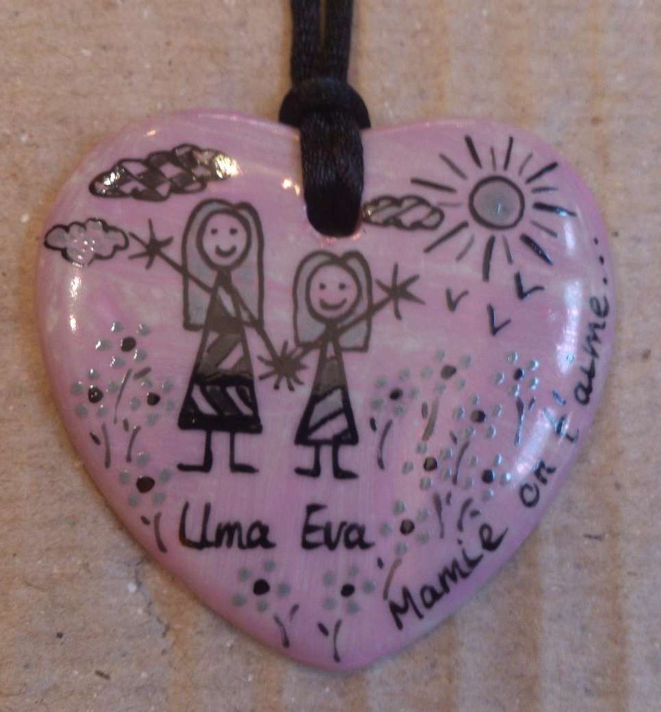 Pendentif coeur personnalisé dans un style naïf en noir et gris sur un fond rose.